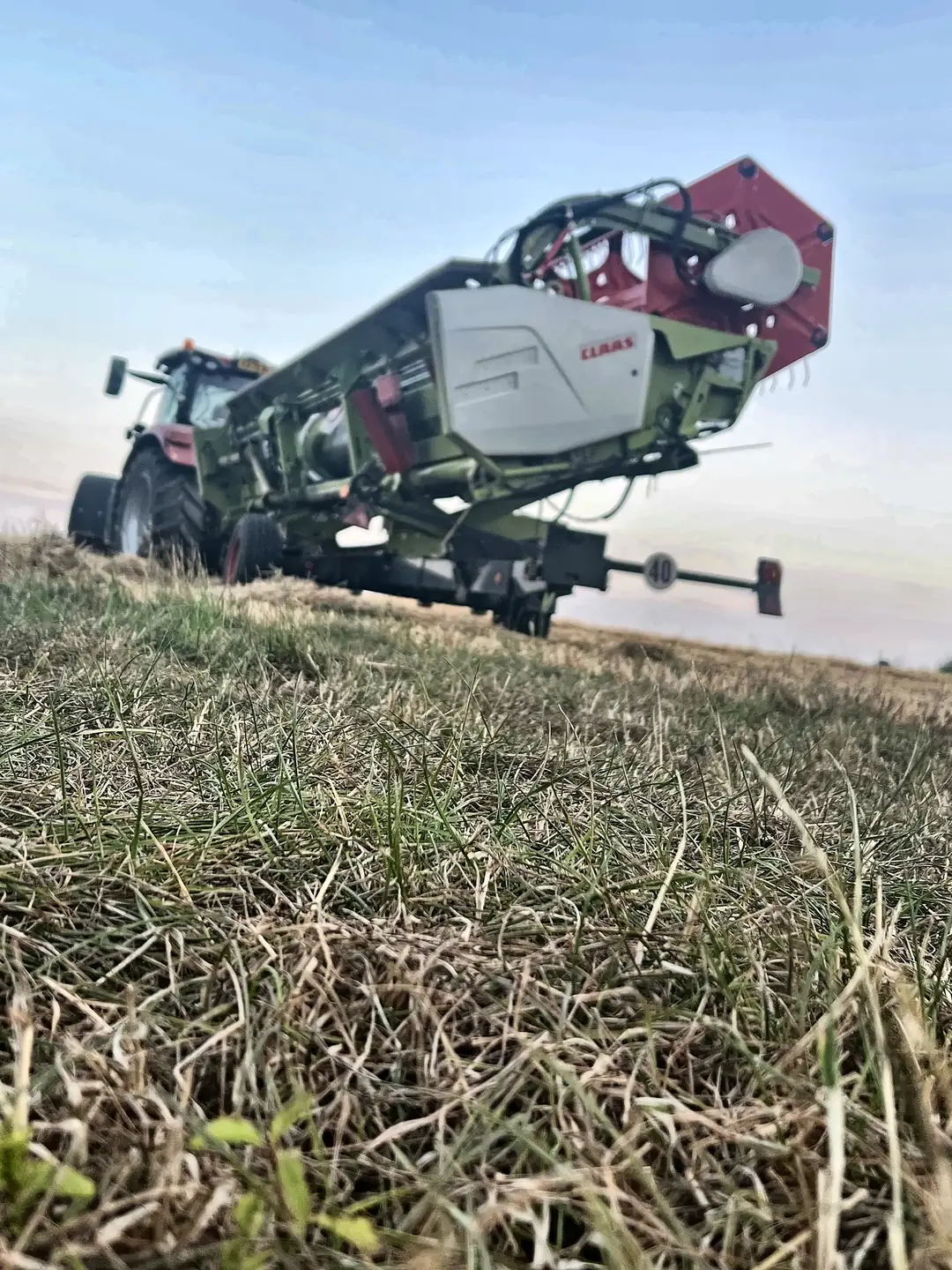 A combine header on its trailer and a tractor left parked in a field at dusk during harvest